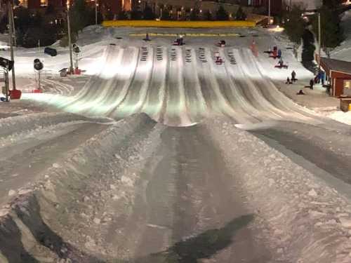 A snowy tubing hill with multiple lanes, people sliding down, and a cozy lodge in the background.