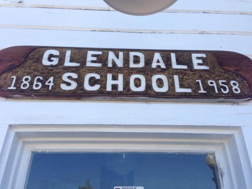 Sign above a door reading "Glendale School 1864 1958" with a wooden background.
