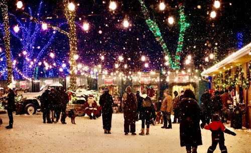 A festive winter scene with people walking in the snow, surrounded by colorful lights and decorations.