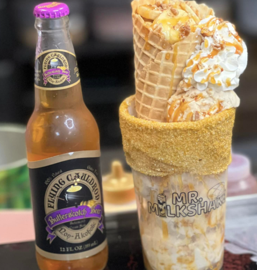 A colorful milkshake topped with whipped cream and a cone, alongside a bottle of butterscotch soda.