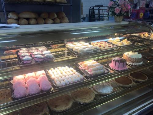 A display case filled with various baked goods, including cakes, pastries, and pies, with bread in the background.
