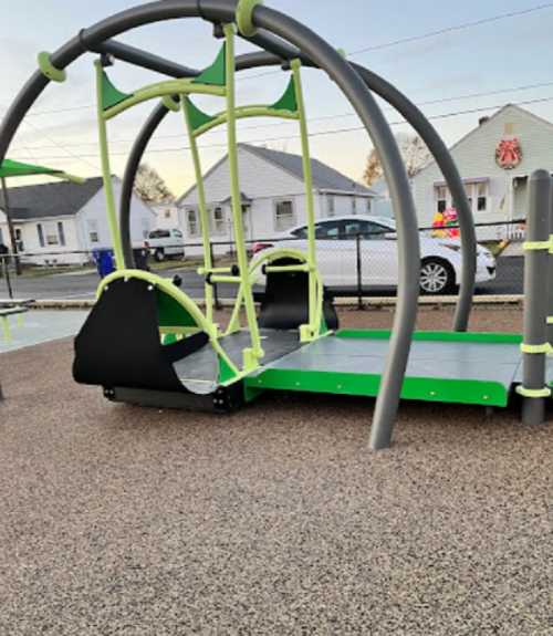 A modern playground structure with green and gray equipment, set on a rubber surface, in a residential area.