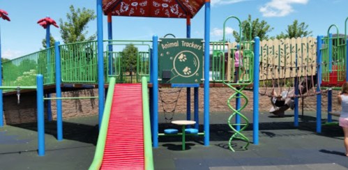 Colorful playground with a slide, swings, and climbing structures under a blue sky.
