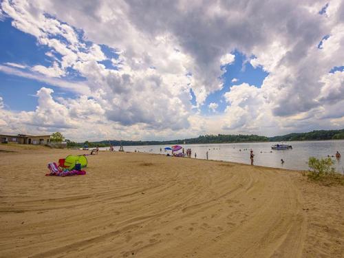 A sandy beach with people swimming and relaxing under a cloudy sky, with boats on the water in the background.