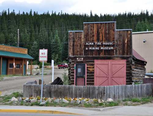 A rustic wooden building labeled "Alma Fire House & Mining Museum" with a "No Parking" sign nearby, surrounded by trees.