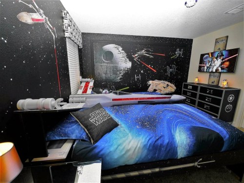 A themed bedroom featuring space decor, a starry bedspread, and wall art of spaceships and planets.