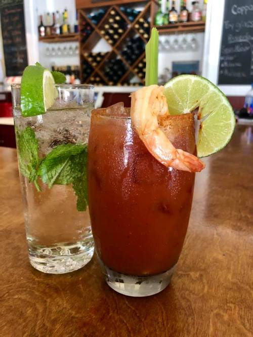 A refreshing mojito and a spicy shrimp cocktail sit on a wooden bar, garnished with lime and mint.