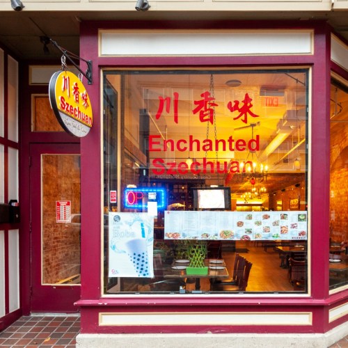 A restaurant window displaying "Enchanted Szechuan" with red lettering and a cozy interior visible.