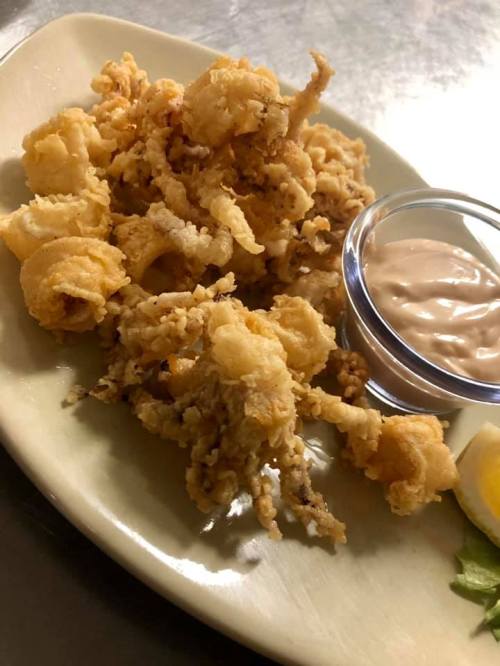 A plate of crispy fried calamari served with a small bowl of dipping sauce and a lemon wedge.