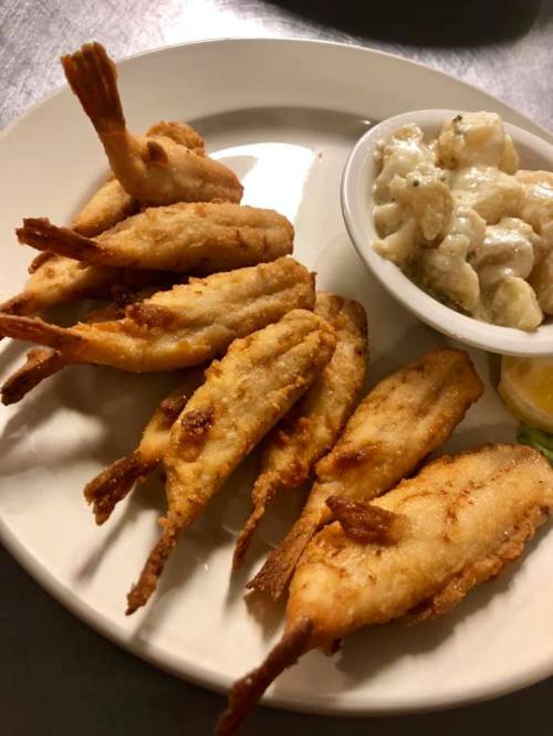 A plate of crispy fried shrimp with a side of creamy dipping sauce and a lemon wedge.