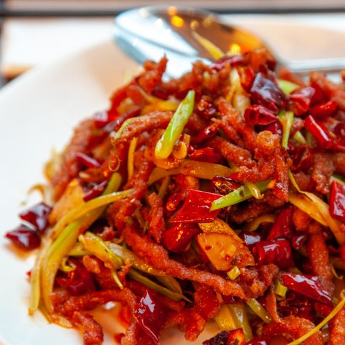A plate of spicy stir-fried shredded meat with green onions and red chili peppers.