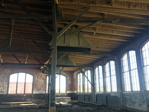 Interior of an abandoned industrial building with large windows and exposed wooden beams.