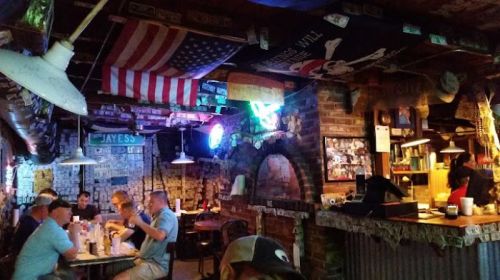A cozy bar interior with flags, neon lights, and patrons enjoying food and drinks at tables.