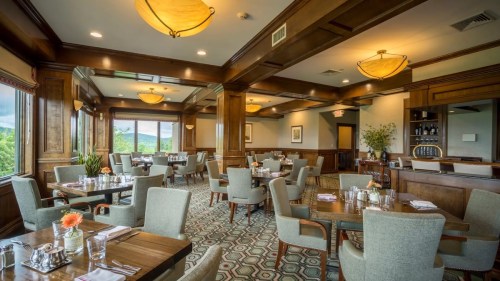 Elegant restaurant interior with wooden accents, tables set for dining, and large windows showcasing a scenic view.