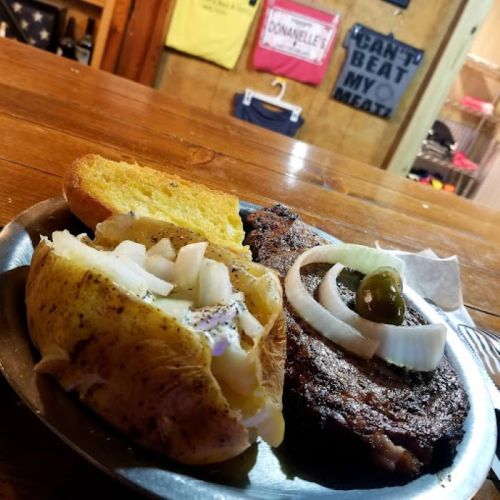 A plate with a baked potato topped with onions and a grilled steak, served on a wooden table.