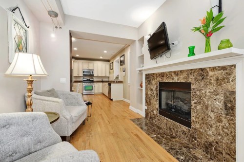 Cozy living room with a fireplace, modern kitchen in the background, and comfortable seating. Bright and inviting atmosphere.