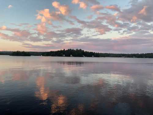 A serene lake at sunset, with soft pink clouds reflecting on the water's surface and a distant island.