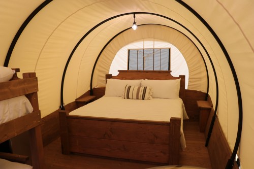 Interior of a cozy glamping tent featuring a double bed and bunk beds, with warm lighting and wooden accents.