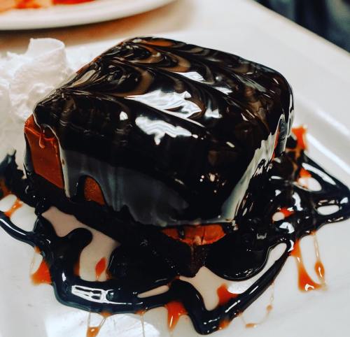 A rich chocolate dessert topped with glossy chocolate sauce and a dollop of whipped cream on a white plate.