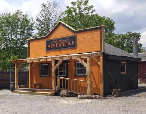 A colorful mercantile building with a wooden porch, surrounded by trees and gravel, under a cloudy sky.