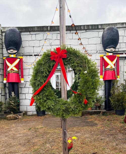A festive wreath with a red bow hangs in front of two toy soldier decorations and a stone wall.