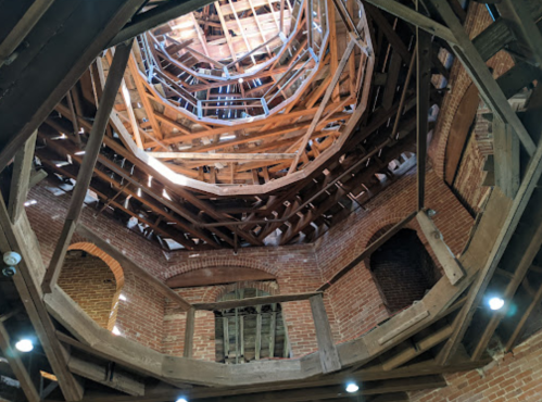 View of a circular wooden structure with exposed beams and brick walls, looking up from the ground level.