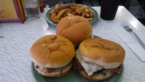 Three burgers on a green plate, with melted cheese and toppings, alongside a plate of golden French fries.