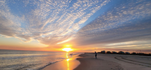 A serene beach at sunset, with vibrant clouds reflecting colors in the sky and gentle waves lapping at the shore.