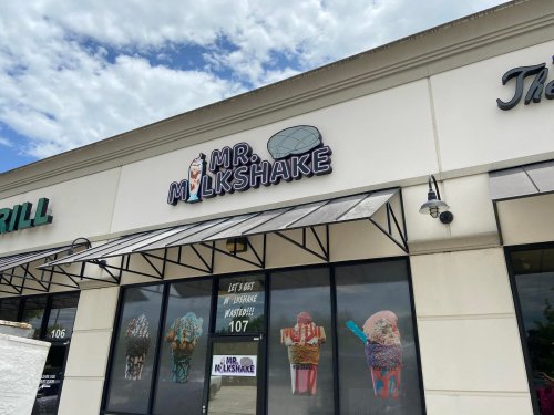 Sign for "Mr. Milkshake" with colorful ice cream cone graphics on a storefront under a cloudy sky.