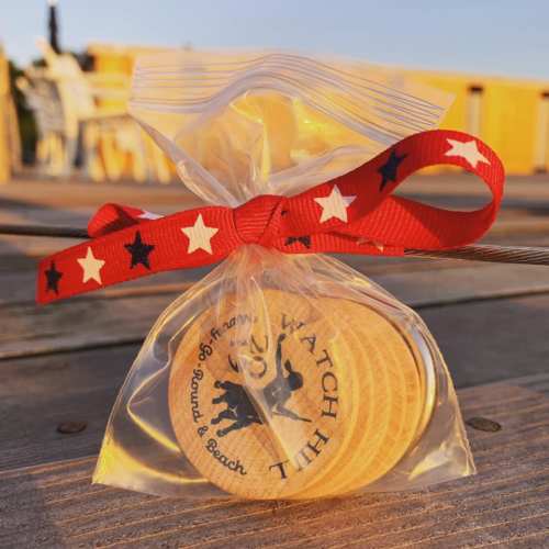 A clear bag tied with a red star-patterned ribbon, containing wooden tokens with a beach-themed design.