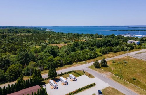 Aerial view of a serene landscape with trailers, greenery, and a lake in the background under a clear blue sky.