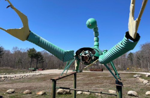 A large, whimsical sculpture of a crab made from metal and pipes, set against a clear blue sky.