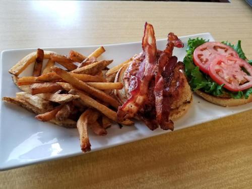 A plate with a bacon burger topped with lettuce and tomato, accompanied by a side of crispy French fries.