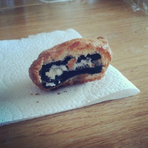 A half-eaten deep-fried Oreo on a paper towel, revealing its creamy filling and chocolate cookie center.