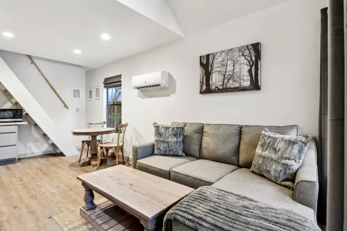 Cozy living room with a gray sofa, wooden table, and air conditioning, featuring a nature-themed wall art.