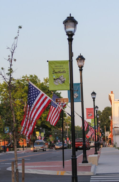 Street view of a downtown area with American flags and decorative banners on lamp posts, lined with trees and buildings.