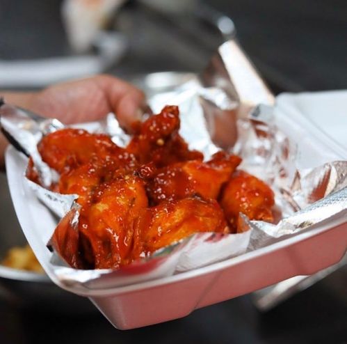 A hand holding a takeout container filled with saucy chicken wings.