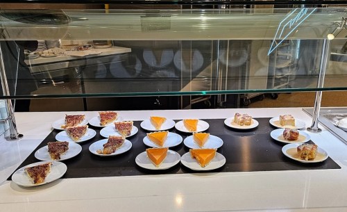 A display of various desserts on white plates, including pie slices and orange cake, arranged neatly on a counter.