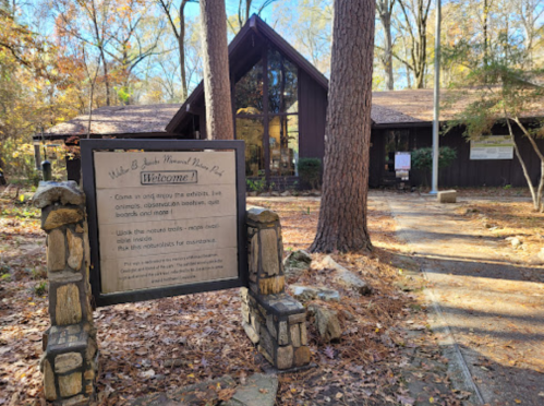 A wooden building surrounded by trees, featuring a welcome sign and a path leading to the entrance.