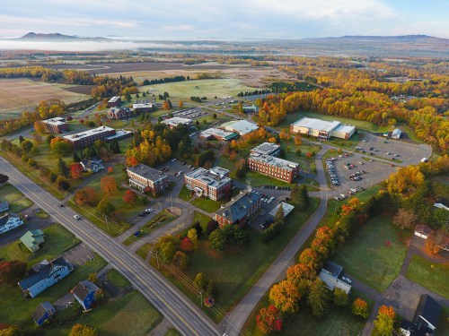 Aerial view of a campus surrounded by colorful autumn trees and fields, with buildings and roads visible.
