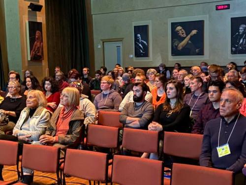 A diverse audience seated in a theater, attentively watching a performance or presentation.