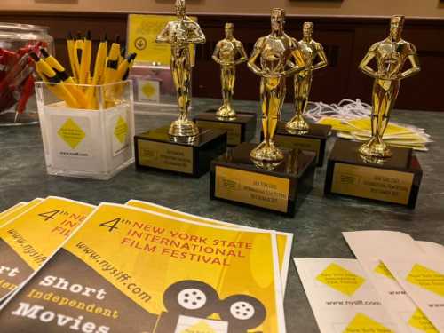 Golden film trophies on a table with promotional materials for the New York State International Film Festival.