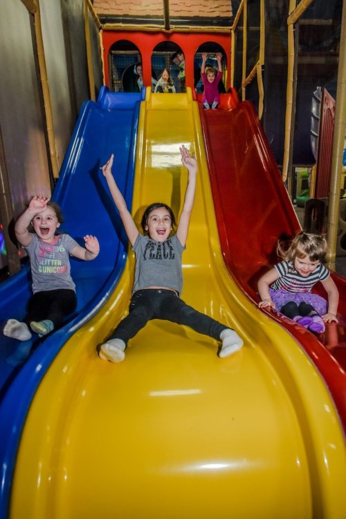 Children joyfully sliding down colorful slides in a play area, with smiles and excitement on their faces.