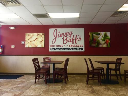 Interior of a restaurant with red walls, tables, and a sign for "Jimmy Buff's" featuring hot dogs and sausages.
