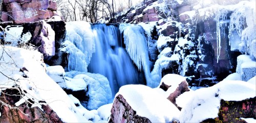 A frozen waterfall surrounded by snow-covered rocks and icicles, creating a serene winter landscape.
