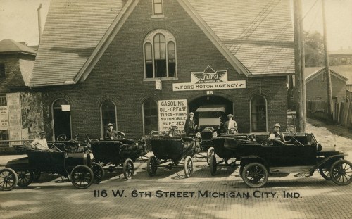 Historic photo of early Ford cars outside the Ford Motor Agency in Michigan City, Indiana, with people posing.
