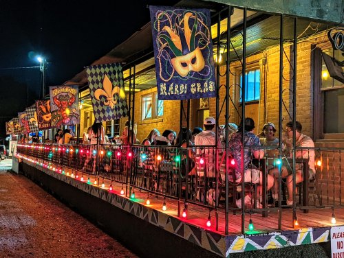 A lively outdoor dining area at night, decorated with colorful flags and lights, with people enjoying their time.