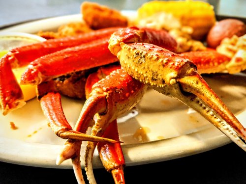 A close-up of a plate featuring cooked crab legs, corn, and other seafood dishes.