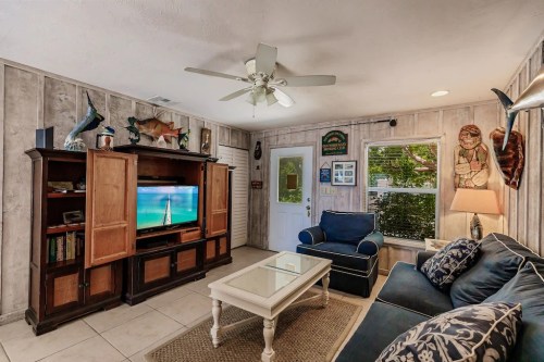 Cozy living room with a blue couch, wooden cabinet, TV, and nautical decor on the walls. Bright and inviting atmosphere.