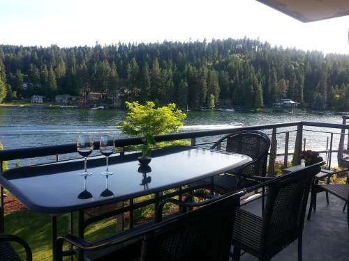 A scenic balcony view overlooking a lake, with a table set for two and lush greenery in the background.